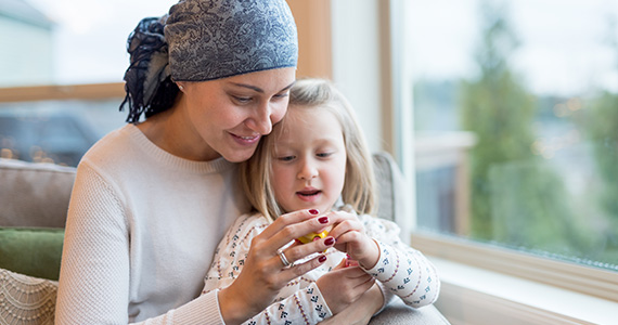 Woman with breast cancer playing with her daughter who is sitting on her lap.